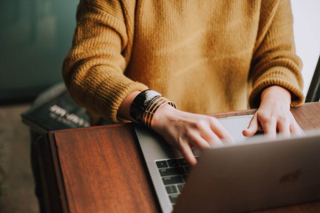 Vrouw in een gele trui zit achter een laptop te typen